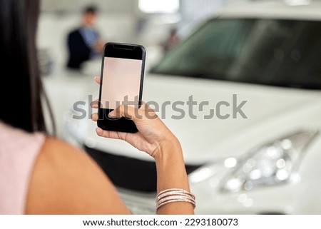Im showing off my new ride on social media. a woman taking picture on her cellphone at a car dealership.