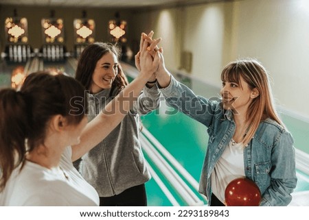 Three young happy women are giving high five and celebrating their score in bowling club.