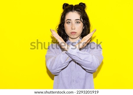 Serious woman making X sign with her arms to stop doing something on yellow background