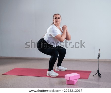 A chubby young woman is watching an online fitness lesson on a mobile phone. Distance sports training Royalty-Free Stock Photo #2293213017