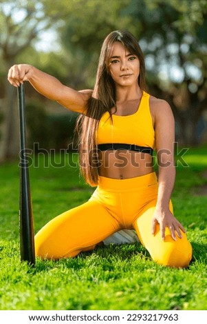 A woman in a yellow sports outfit holds a baseball bat in her hand.