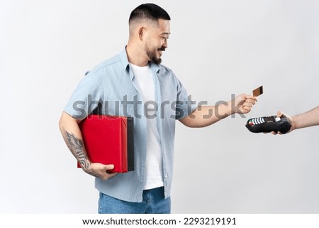 Portrait of handsome smiling asian man parcel, holding credit card making payment using credit card machine, isolated on white background . Wireless technology concept