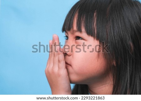 Little asian girl covering her mouth to smell the bad breath. Child girl checking breath with her hands. Oral health problems or dental care concept. Royalty-Free Stock Photo #2293221863