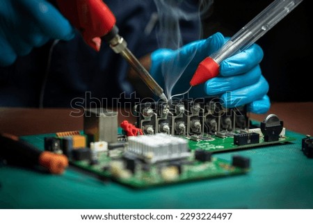 A male technician in gloves is soldering circuit board of CCTV camera. Repairman in workshop Royalty-Free Stock Photo #2293224497