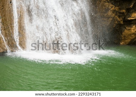 Beautiful waterfall in forestry with blue water with ripples on the surface. Blurred transparent blue colored clear calm water surface texture with splashes and bubbles. Water waves with shining.