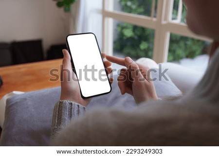 Close up woman hand holding a smartphone blank white screen sitting on sofa at home
