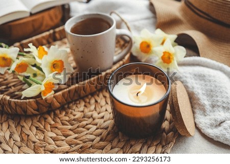 Cozy spring composition, burning candle, daffodils and hat.