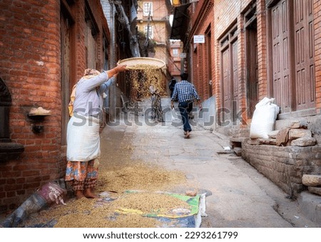 A woman sifting the chaff out of the rice in the old city of Bhaktapur Nepal. Royalty-Free Stock Photo #2293261799