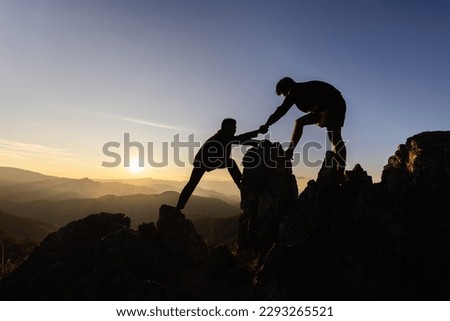 Silhouette Teamwork, Male hikers climbing up mountain cliff and one of them giving helping hand. People helping and, team work concept.