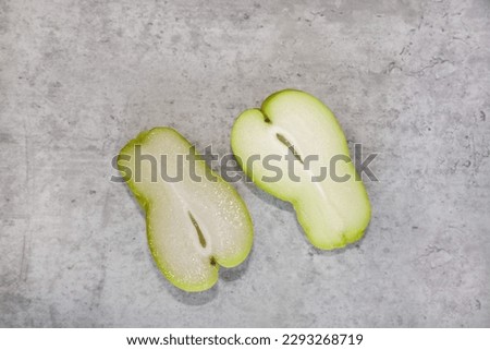 Top view of a chayote squash cut in half with view of the edible seed in the middle.