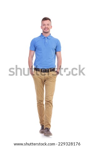 full length picture of a young casual man walking toward the camera with his hands in his pockets while smiling. isolated on a white background