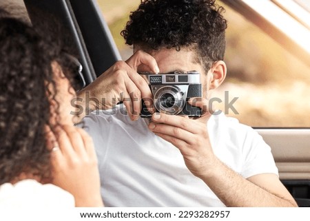 The best memories are the ones made on road trips. a young man taking a picture of his girlfriend while sitting in a car together.