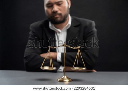 Focus golden scale balance with burred background of lawyer in black suit sit on his office desk, symbol of legal justice and integrity, balanced and ethical decision in court of law equility