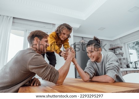 Father competing in arm wrestling with teenager son, family spending time together. Dad and children having fun at home. 