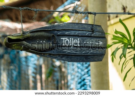 Black flippers with an inscription toilet in the form of a sign with a pointer, which is suspended on rope in a tropical beach cafe, close up, Thailand. Creative concept, the inscription