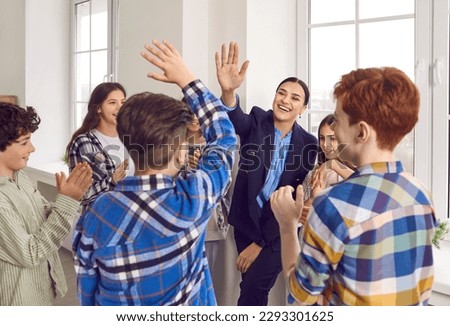 Group of children and their teacher having fun in the classroom. Happy woman teacher gives a high five to a student boy while others are clapping their hands. Support and teamwork at school concept Royalty-Free Stock Photo #2293301625