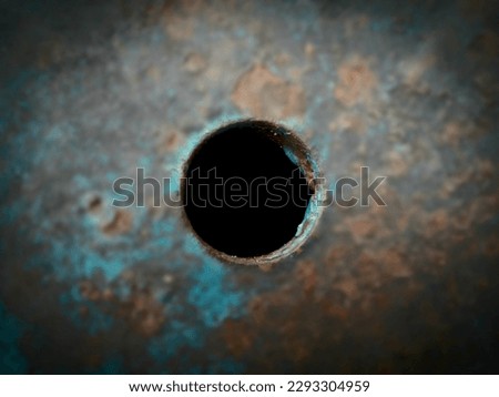 Photo of a small black, deep hole in an iron plate found in a junkyard