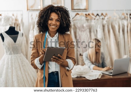A beautiful wedding dress designer holds a tablet and looks at the camera Royalty-Free Stock Photo #2293307763