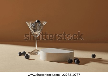 A cocktail glass filled with blueberries displayed with a white round podium. Salicylic acid in Blueberry kills all those acne-causing bacteria that cause skin to break out