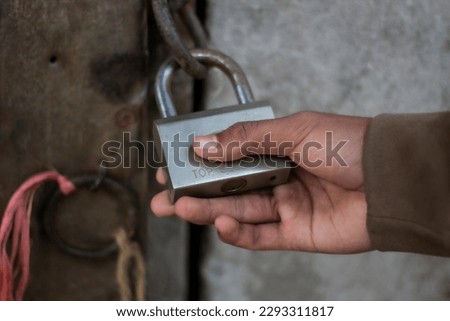 A lock hangs on a door and a person holds the lock