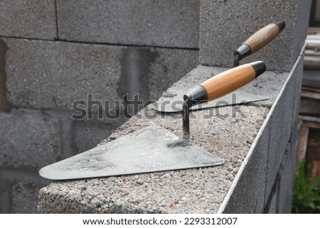 The concrete worker's trowels lie on a cinder block construction stone. It is used for bricklaying, as well as for measuring and applying cement mortar Royalty-Free Stock Photo #2293312007