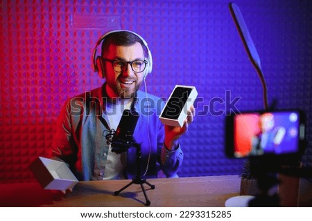 Young male technology blogger recording video blog or vlog about new smartphone and other gadgets at home studio. Blogging, Work from Home concept. Focus on gadgets at the table. Web Banner. Royalty-Free Stock Photo #2293315285