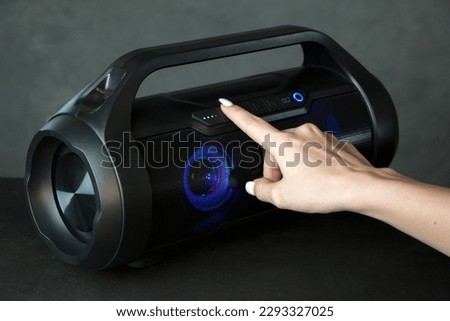 Wireless bluetooth column on a grey background. The female hand presses to play, pause, accept. High quality photo