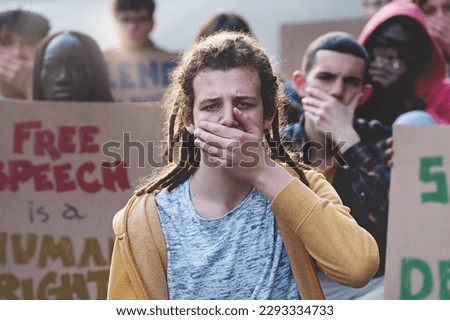 Students Protesting for Free Speech: Group outdoors, covering mouths, holding signs (e.g., "free speech is a human right"), with focus on blond teenager with dreadlocks. Royalty-Free Stock Photo #2293334733