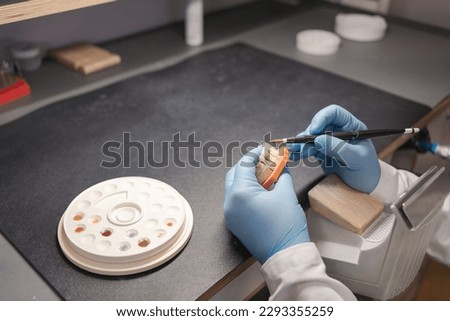 Technician dental is working with complete lower and upper metal ceramic prosthesis dental. Dental technician works by brush with jaw model Royalty-Free Stock Photo #2293355259