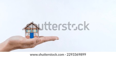 A woman's hand holds a mock-up or miniature of a residential building, white isolated background. Purchase and sale of real estate, construction of a residential building.
