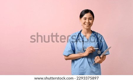 Young beautiful female doctor writing on tablet while standing on pink isolated background. 