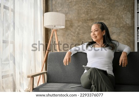 Middle aged woman relaxing in her free time sitting on the sofa at home. retirement life concept Royalty-Free Stock Photo #2293376077