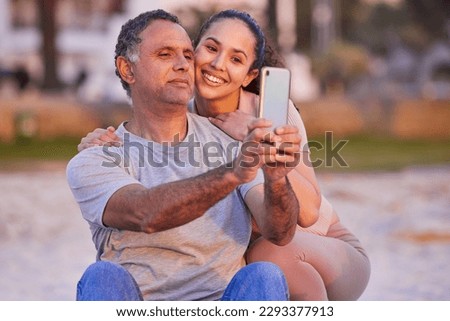 She taught me how to take selfies. a mature man using a cellphone to take selfies with his daughter during a day on the beach.
