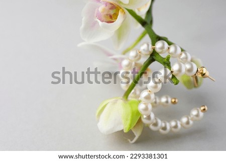 Elegant pearl earrings and orchid flowers on white background, closeup. Space for text