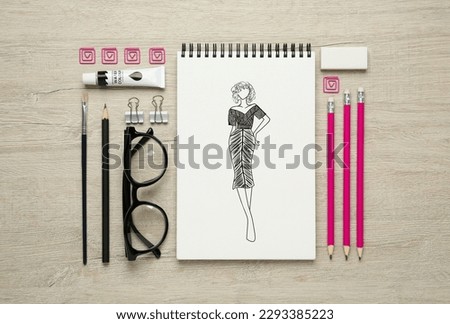 Sketch of stylish clothes in pad on wooden table. Fashion designer's desk with stationery, flat lay
