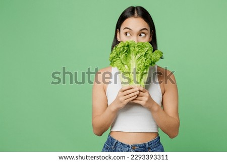 Young woman wear white clothes hold cover mouth with bunch of fresh greens lettuce leaves look aside isolated on plain pastel light green background. Proper nutrition healthy fast food choice concept