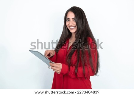 Photo of happy cheerful young brunette woman wearing red shirt over white studio background hold tablet browsing internet