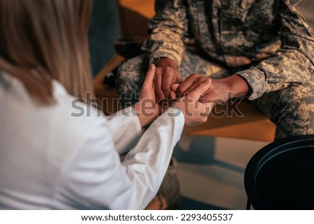 A soldier is in therapy at the psychologist office, holding hands with her in the process of rehabilitation. Royalty-Free Stock Photo #2293405537