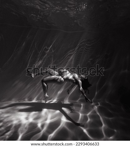 Underwater shoot of beautiful pregnant woman swimming in water through sunbeams. Fantasy mermaid against water background with rays of lights. Black and white image.