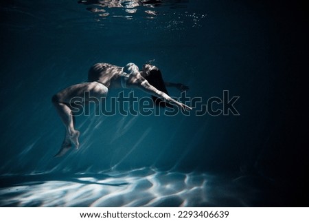 Underwater shoot of beautiful pregnant woman swimming in water through sunbeams. Fantasy mermaid against turquoise water background with rays of lights.