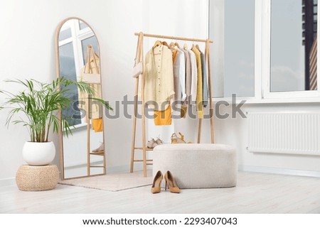Stylish dressing room interior with mirror, ottoman and clothing rack Royalty-Free Stock Photo #2293407043