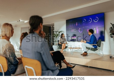 Two diverse young adult lecturers are in a conference room having a panel discussion in front of a full auditorium. Royalty-Free Stock Photo #2293417531