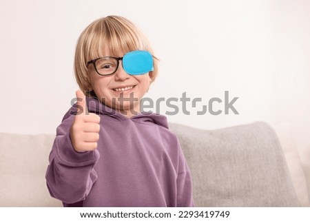 Happy boy with nozzle on glasses for treatment of strabismus showing thumbs up in room. Space for text Royalty-Free Stock Photo #2293419749