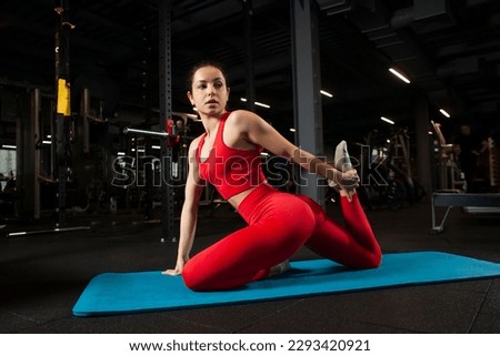 athletic woman in red sportswear sitting on yoga matte in black gym and warming up, girl doing yoga and stretching, attractive woman in fitness club doing flexibility exercise Royalty-Free Stock Photo #2293420921