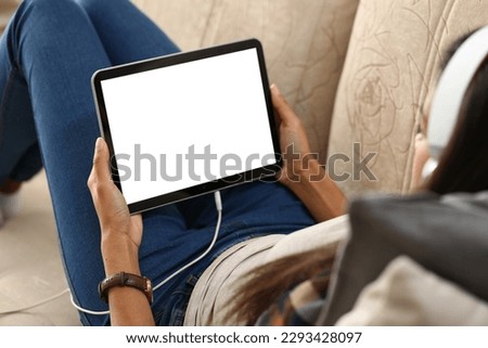 Mockup image of a digital tablet with black screen in hands of woman in headphones