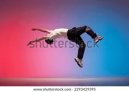 guy acrobat doing back fat in new lighting, male dancer jumps and falls in the air on red blue background, hiphop performer does trick and levitates in the air Royalty-Free Stock Photo #2293429395