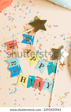Colorful Happy birthday flags garland on a beige background with confetti, copy space