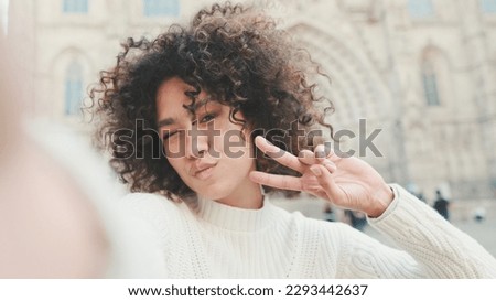 Young woman is sitting down on a cell phone. Girl showing victory sign posing for a selfie on the old city background