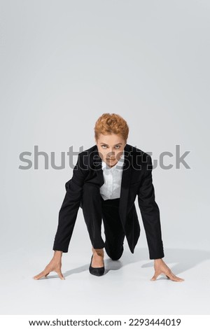 full length of purposeful businesswoman in black suit looking at camera from low start position on grey background