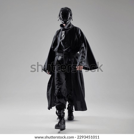 Urbantech outfit cyber style, a young man in stylish black clothes and a mirror mask on the whole face, futuristic style. Studio photo on a light background Royalty-Free Stock Photo #2293451011
